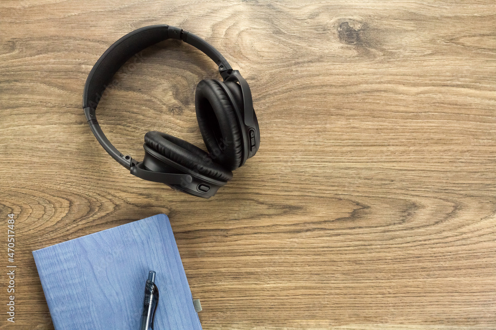 Overhead view of wireless headphones and notebook with pen on a wooden table. Top down view of black over ear headphones on a wooden table Overhead view of wireless headphones and notebook with pen on a wooden table. Top down view of black over ear headphones on a wooden table