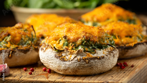 Soft cheese and spinach stuffed mushrooms with cheesy crust served on rustic wooden board, vegetarian food. photo