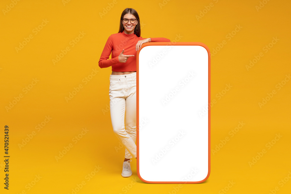 Young woman standing and showing with finger blank screen of huge phone, mockup for your app - obrazy, fototapety, plakaty 