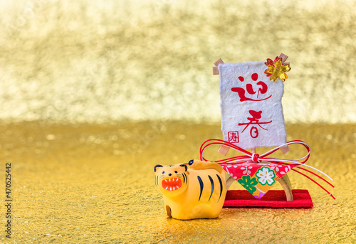Japanese New Year's Card depicting a cute Zodiacal animal figurine of the tiger for 2022 in front of handwritten ideograms Geishun or Welcoming Spring on traditional decoration on a golden background. photo