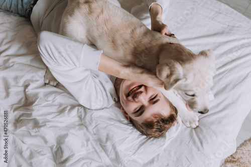 teen boy is lying in bed on white bedding with dog. top view. pet wakes up the owner in the morning. space for text. High quality photo