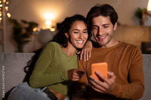 Cheerful Couple Using Cellphone Sitting On Couch At Home
