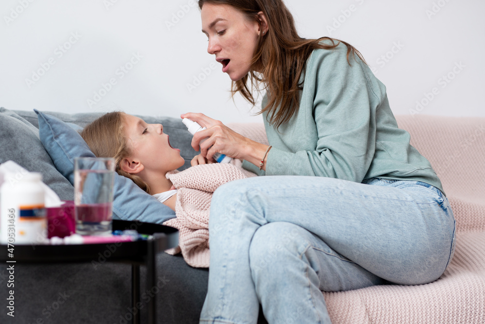 Girl has a sore throat and her mother sprays her medicine