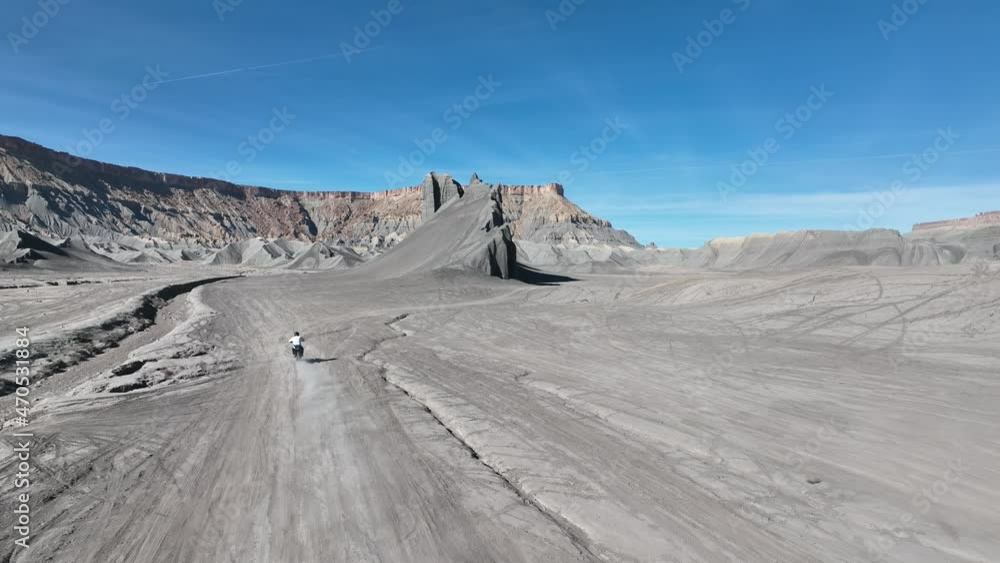 Dirt Biker riding toward unique mountain in blue shale desert Dirt Biker riding toward unique mountain in blue shale desert