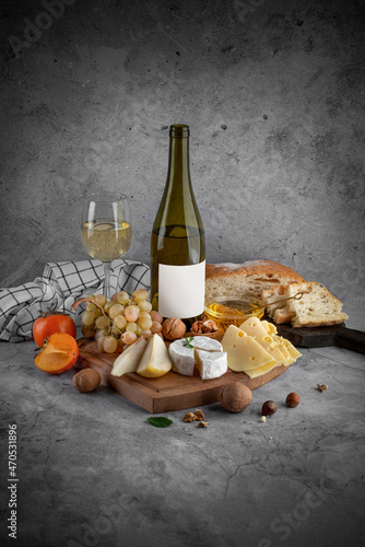Board with cheese, bottle of wine and fruits on grey background