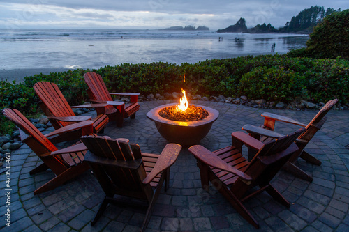 Adirondack chairs around a fireplace facing the beach of Cox Bay in Tofino Vancouver Island Canada. People are walking on the beach photo