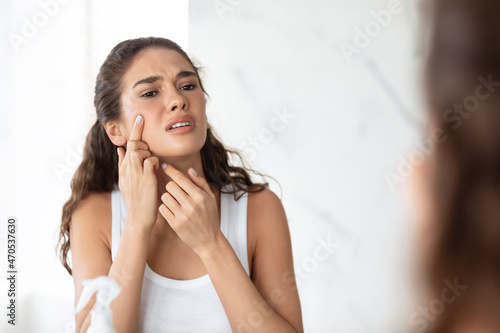 Desperate Lady Squeezing Pimple On Face Near Mirror In Bathroom