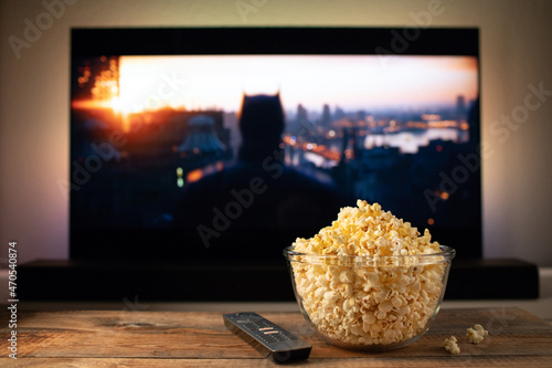 A glass bowl of popcorn and remote control in the background the TV works. Evening cozy watching a movie or TV series at home photo