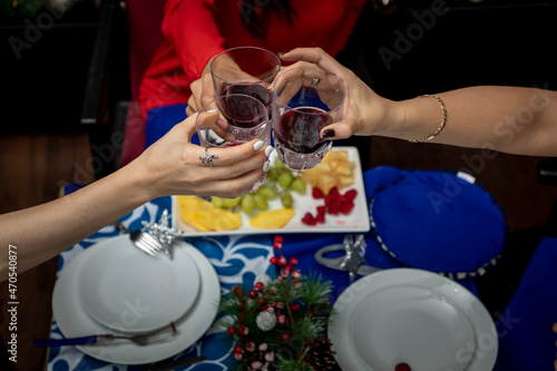 top view of hands with glasses toasting at a christmas dinner, with christmas decoration in the background