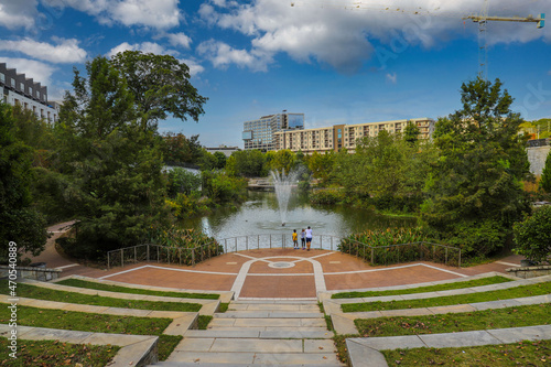 a gorgeous shot of the green lake with water fountain in the center of the water, green and autumn colored trees with African American people standing near the lake at Historic Fourth Ward Park