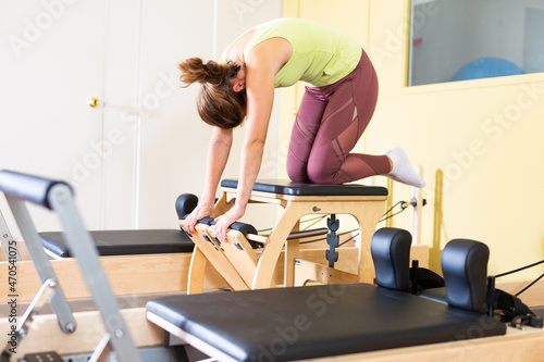 Concentrated young woman practicing pilates stretching exercises on combo chair. Healthy lifestyle and fitness concept..