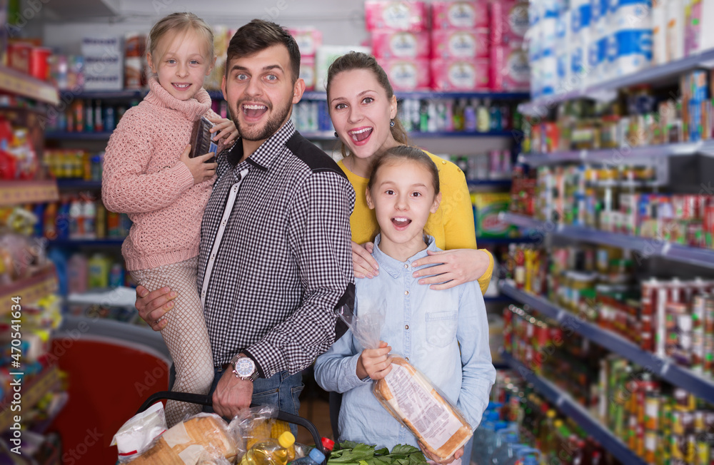 smiling parents with two little girls with purchases during family shopping in grocery store