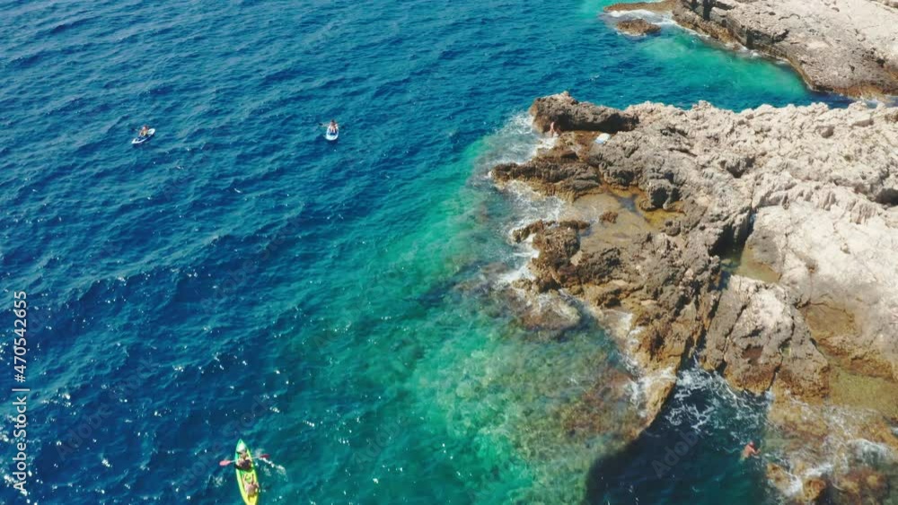 Sportsmen sail bright kayak and people on SUP surfboards in tranquil sea lagoon near limestone rocky beach on sunny day aerial view Sportsmen sail bright kayak and people on SUP surfboards in tranquil sea lagoon near limestone rocky beach on sunny day aerial view
