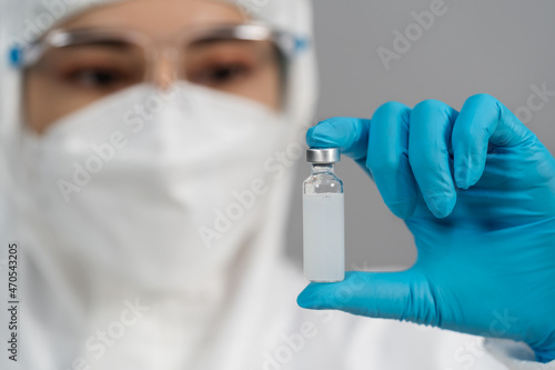 doctor in PPE suit holding and gently shaking vaccine bottle