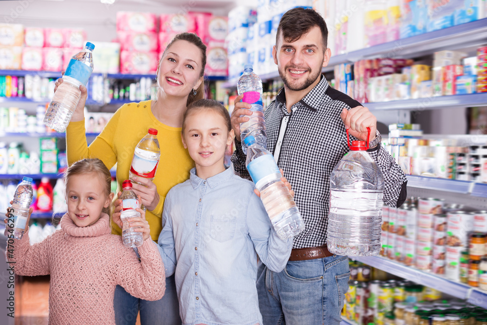 Positive friendly family of four with bottles of water in supermarket