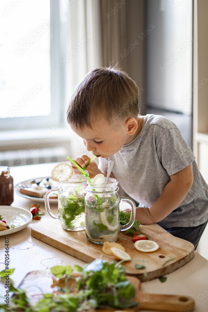 Cute little boy trying fresh homemade lemonade from jar use straw enjoying taste at modern kitchen Cute little boy trying fresh homemade lemonade from jar use straw enjoying taste at modern kitchen