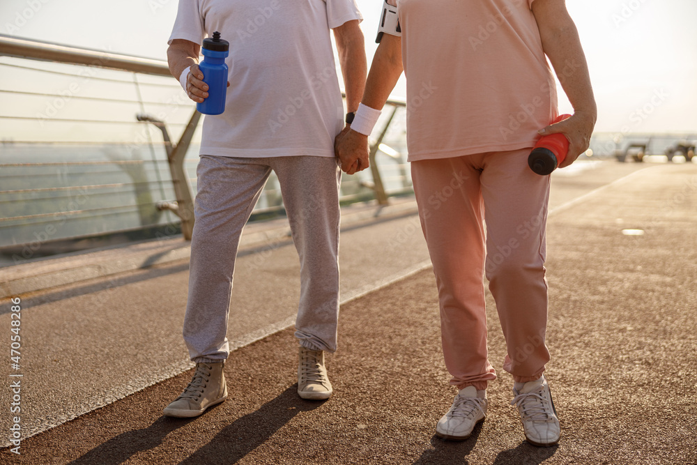 Mature couple in sportswear with bottles stands on city footbridge in evening