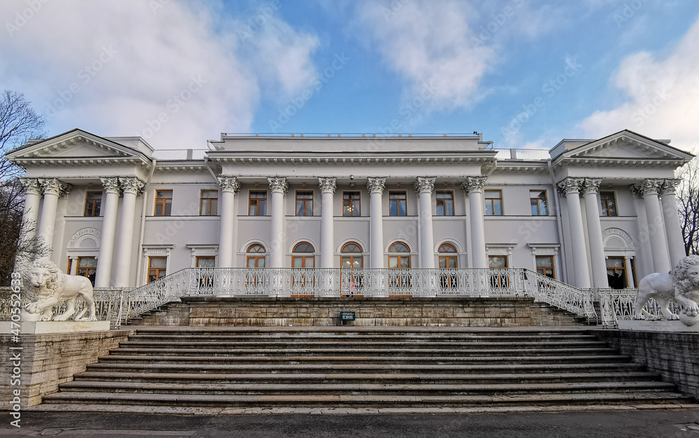 The entrance to the Elaginoostrovsky Palace with a staircase and white lions against a blue sky with clouds