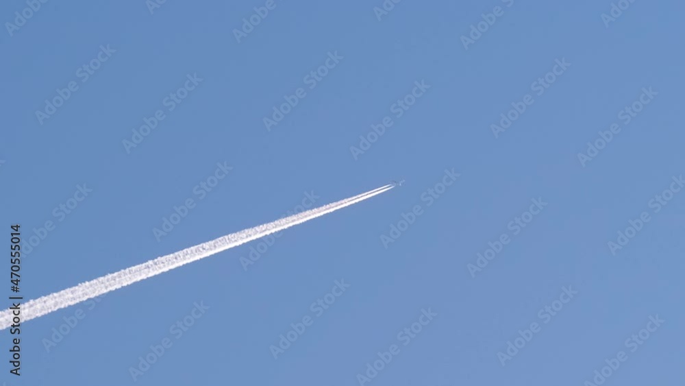 Distant passenger jet plane flying on high altitude on clear blue sky leaving white smoke trace of contrail behind. Air transportation concept Distant passenger jet plane flying on high altitude on clear blue sky leaving white smoke trace of contrail behind. Air transportation concept
