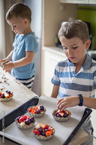 Cute baby boys preparing homemade sweet dessert serving with fruit and berries before baking