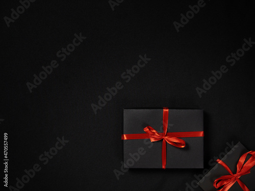 Black package with red satin leeta on dark background, view from the top, space for text