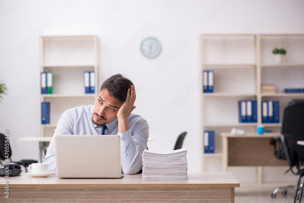 Young male employee unhappy with excessive work in the office Young male employee unhappy with excessive work in the office