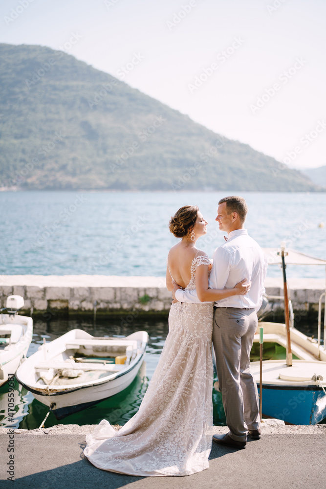 Bride and groom stand on the pier, looking at each other near the parking lot of boats