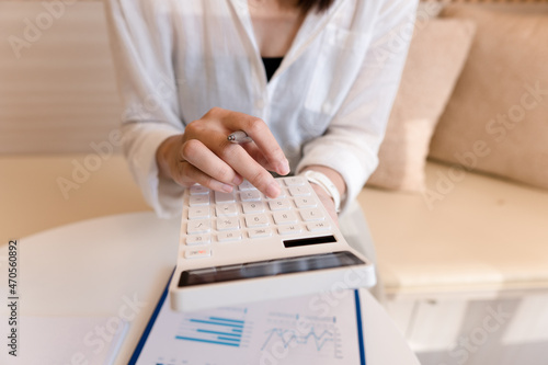 businesswoman using calculator while sitting at workplace with graphs and charts.