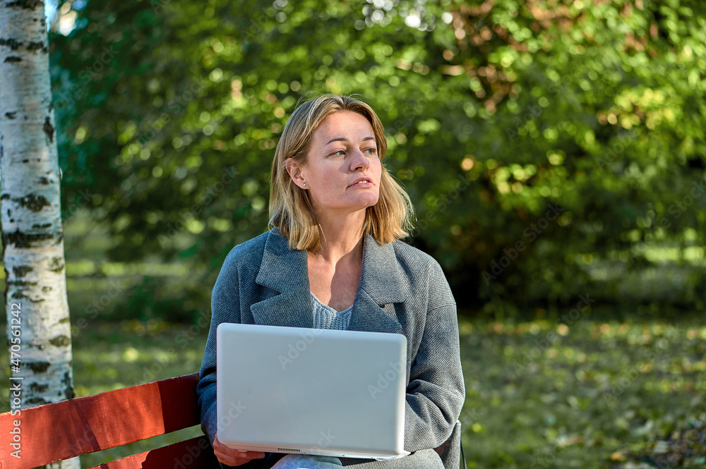 A woman with a laptop is sitting on a park bench on a sunny summer day A woman with a laptop is sitting on a park bench on a sunny summer day