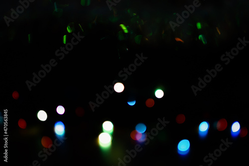 Multi-colored bokeh on a black background. Bright blurry textures of holiday lights. Colorful beautiful Christmas garlands on blurry background. Layout of a greeting card for the New year. Copy space