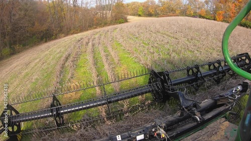 POV of farmer using a combine and a belted soybean header to harvest beans in field in the Medwest; field surrounded by colorful trees; concepts of circle of life, harvest, hard work and farm life photo