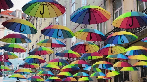 Rainbow colored umbrellas dangle over pink street in Lisbon Portugal