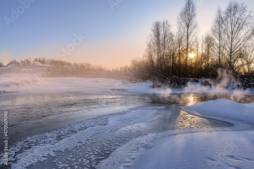 Foggy frosty morning with the rising sun on the Neiva River (Ural, Russia) in winter. The river freezes and becomes covered with ice patterns in the form of stars. Stoves in houses are fired  © olgaS
