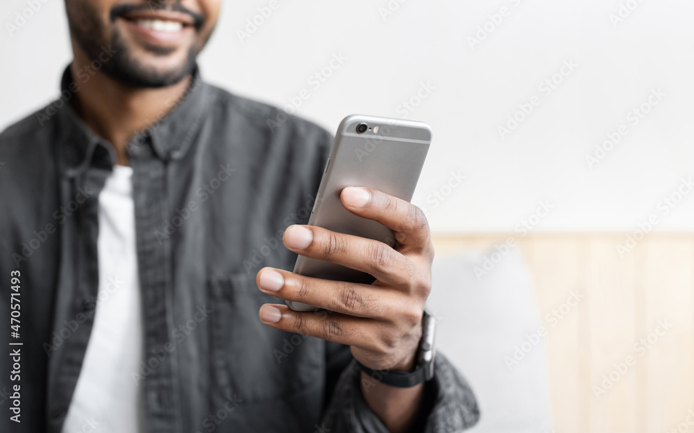 Young smiling man looking at mobile phone at home, male hand with smartphone closeup
