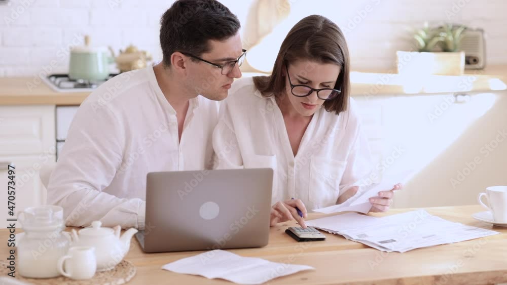 Young woman, man working with documents and sitting at table with laptop in home office spbi. Closeup view of beautiful couple talks and does job with paper project, calculates and sits at desk in Young woman, man working with documents and sitting at table with laptop in home office spbi. Closeup view of beautiful couple talks and does job with paper project, calculates and sits at desk in