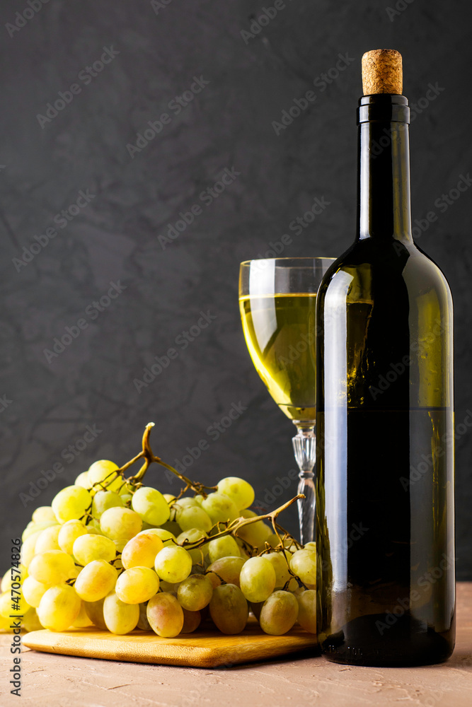Obraz premium a glass glass and a bottle of white wine and a brush of white grapes on a cutting board on a black background