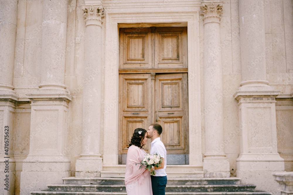 Groom kisses bride on the forehead against the background of the facade of the building