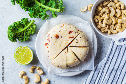 Vegan cashew cheese with dried tomatoes and spices on white plate, gray background. Alternative dairy-free diet, vegan food. photo