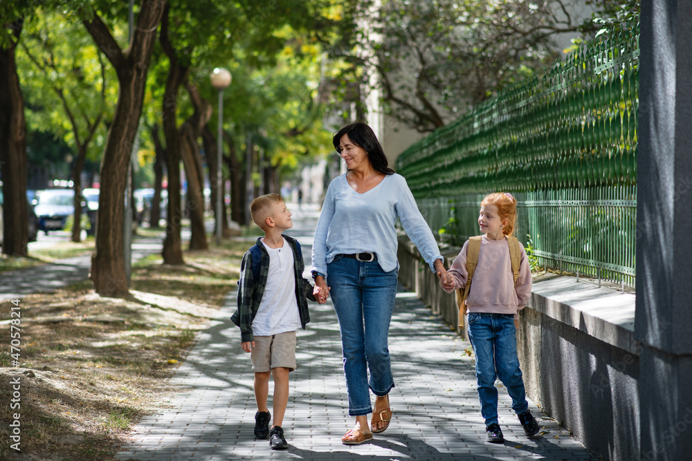 Happy grandmother taking grandchildren home from school, walking outdoors in street. Happy grandmother taking grandchildren home from school, walking outdoors in street.