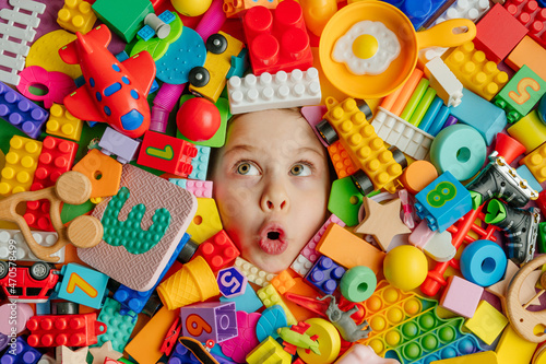 Funny surprised little girl lying in the chaos of toys