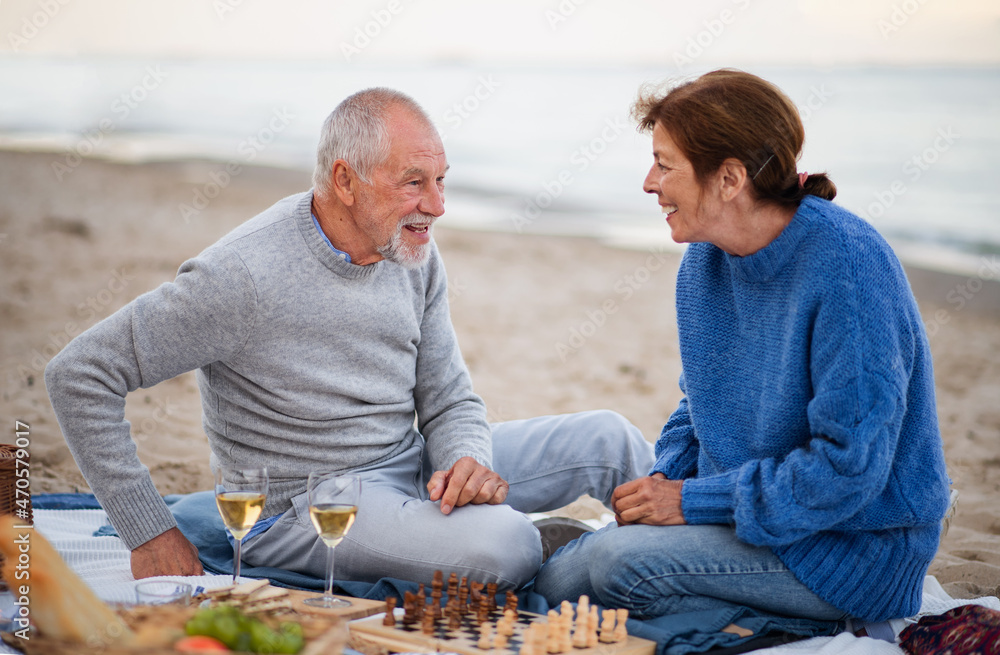Happy senior couple in love sitting on blanket drinking wine and playing chess outdoors on beach. Happy senior couple in love sitting on blanket drinking wine and playing chess outdoors on beach.
