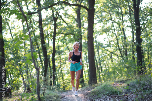 Happy active senior woman jogging outdoors in forest. © Halfpoint