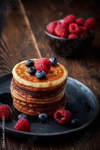 Tasty appetizing homemade pancakes served with honey and raspberries on plate on dark background