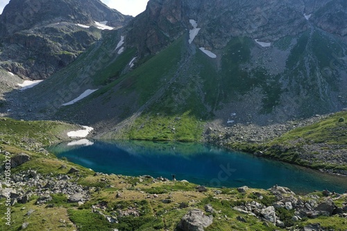 Aerial view of man traveler tourist standing alone near Seven colored lake in mountains, summer landscape: high peaks, snow, stones, colorful mountain lake. Arkhyz Caucasus, Karachay-Cherkessia Russia