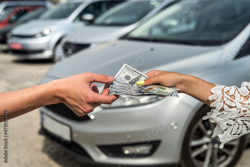 female hand gives dollar to a salesman when buying a new modern car © RomanR
