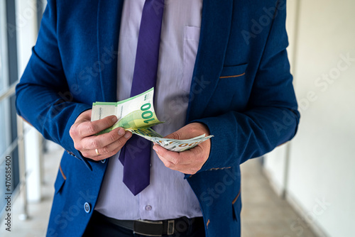 man wear blue suit holding euro and dollars bills