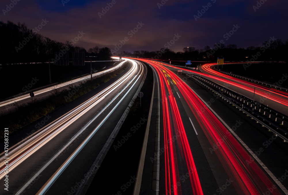 Night view of German Autobahn “A40“ in Ruhr Basin Germany in Duisburg-Kaiserberg near Oberhausen, Essen and Duesseldorf. Panoramic longtime exposure with red and white lights of passing cars at dusk.