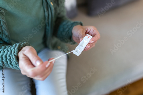 Shot of a woman using cotton swab while doing coronavirus PCR test. Woman takes coronavirus sample from her nose at home. Senior woman at home using a nasal swab for COVID-19.