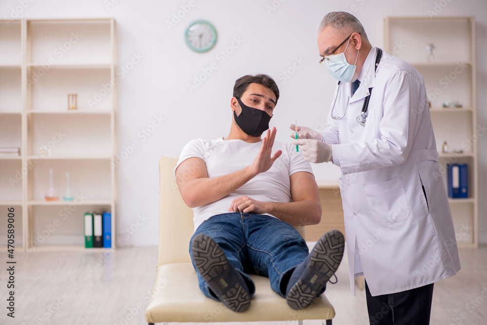 Fototapeta premium Young male patient visiting old doctor in vaccination concept