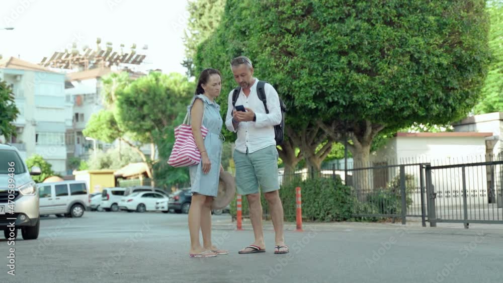 Couple of tourists using smart phone gps in street search locations. A woman and a man use the online map in their smartphone to search. Couple of tourists using smart phone gps in street search locations. A woman and a man use the online map in their smartphone to search.